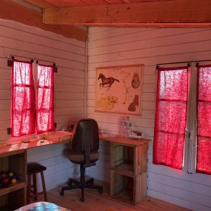 Cabane en bois avec des rideaux rouges, bureau en bois et ambiance chaleureuse.