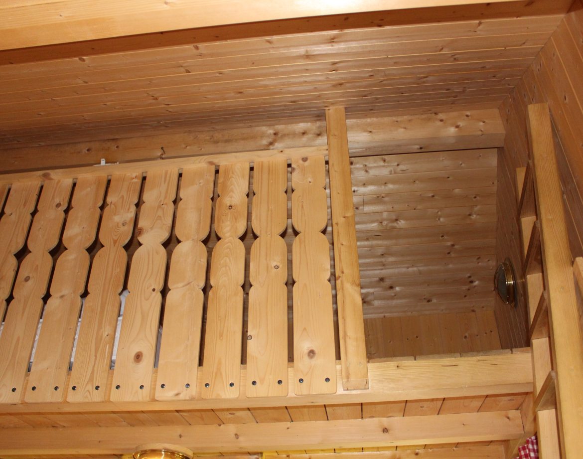 Cabane en bois avec un intérieur chaleureux, balustrade en bois sculpté et plafond en lambris.