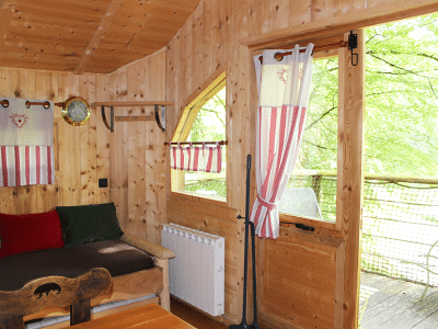 Intérieur chaleureux d'un chalet en bois, avec des rideaux rayés et une vue sur la nature.