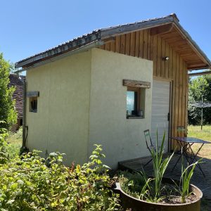 Cabane en bois avec terrasse, entourée de verdure et d'un jardin fleuri.
