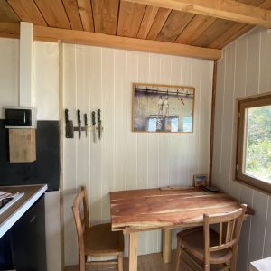 Intérieur d'une cabane en bois, avec une table en bois, des chaises et une cuisine équipée.