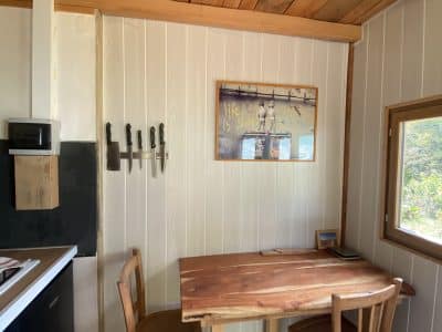 Intérieur d'une cabane en bois, avec une table en bois, des chaises et une cuisine équipée.