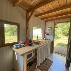 Cabane en bois avec cuisine lumineuse, vue sur la nature et accès à une terrasse.