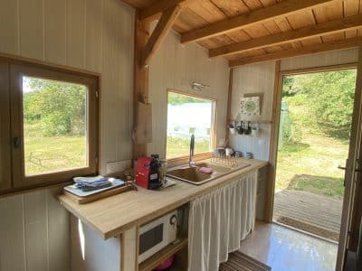 Cabane en bois avec cuisine lumineuse, vue sur la nature et accès à une terrasse.