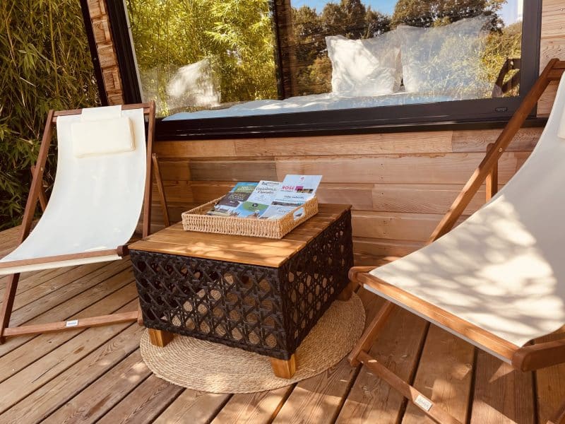 Chalet en bois avec chaises longues et table en osier sur une terrasse ensoleillée.
