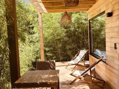 Cabane en bois avec terrasse ensoleillée, chaises longues et vue sur un jardin de bambous.