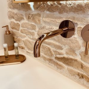 Salle de bain moderne avec robinet en cuivre et mur en pierres naturelles, ambiance chaleureuse.