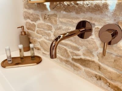 Salle de bain moderne avec robinet en cuivre et mur en pierres naturelles, ambiance chaleureuse.