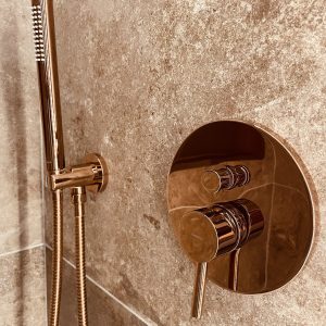 Douche moderne en hébergement insolite, avec robinetterie en cuivre et carrelage élégant.