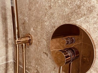 Douche moderne en hébergement insolite, avec robinetterie en cuivre et carrelage élégant.