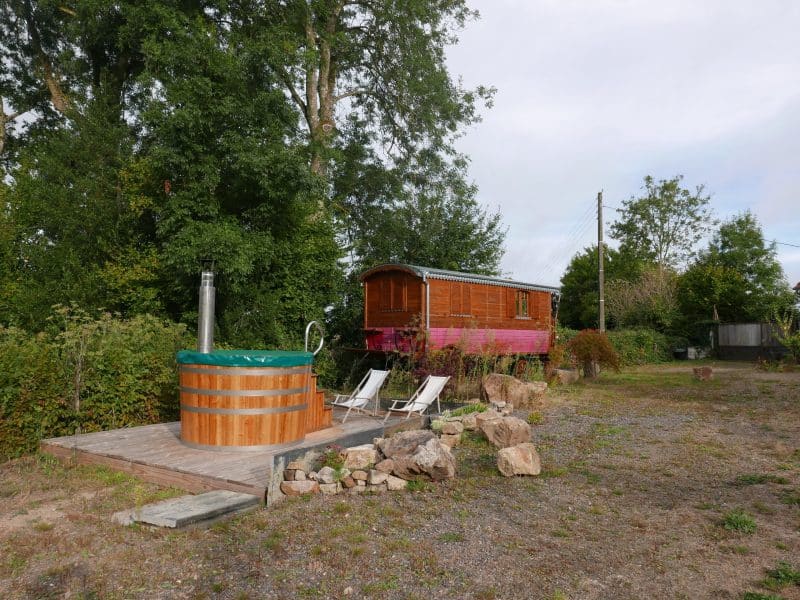 Roulotte en bois avec jacuzzi extérieur et chaises longues dans un cadre verdoyant.
