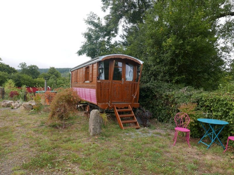 Charmante roulotte en bois, entourée de verdure, avec une terrasse colorée.