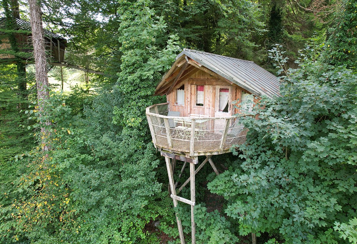 Cabane perchée dans les arbres, avec un balcon en bois entouré de verdure luxuriante.