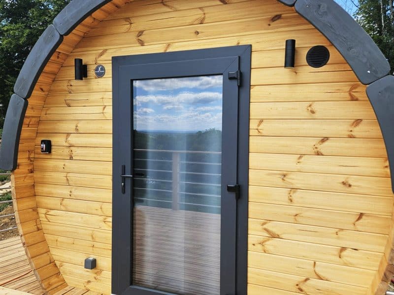 Cabane en bois en forme de tonneau, avec une porte vitrée et un balcon en bois.