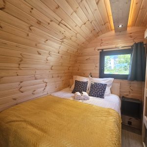 Cabane en bois chaleureuse avec lit douillet, décorée de coussins élégants et d'une lumière douce.