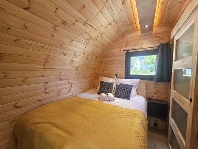 Cabane en bois chaleureuse avec lit douillet, décorée de coussins élégants et d'une lumière douce.