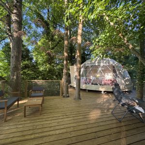 Dôme géodésique en pleine nature, avec terrasse en bois et coin détente ombragé.