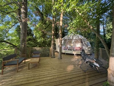 Dôme géodésique en pleine nature, avec terrasse en bois et coin détente ombragé.