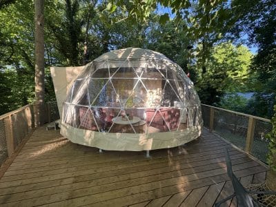 Dôme transparent en pleine nature, avec terrasse en bois et mobilier cosy pour un séjour unique.