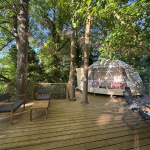 Dôme géodésique en pleine nature, avec terrasse en bois et chaises confortables.