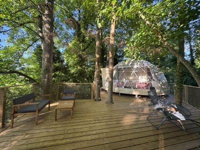 Dôme géodésique en pleine nature, avec terrasse en bois et chaises confortables.