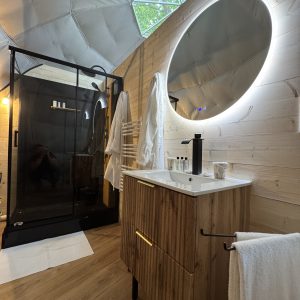 Salle de bain moderne dans une yourte, avec douche vitrée et miroir lumineux.