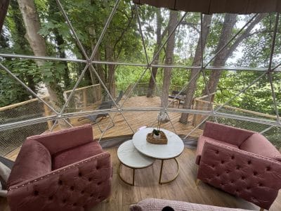 Dôme transparent avec vue sur la nature, salon cosy et mobilier moderne. Parfait pour se détendre.