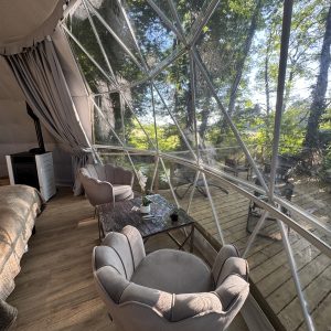 Dôme transparent avec vue sur la nature, fauteuils confortables et ambiance chaleureuse.