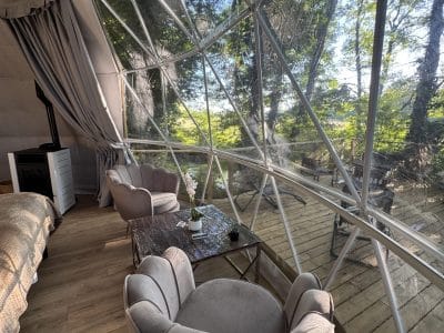 Dôme transparent avec vue sur la nature, fauteuils confortables et ambiance chaleureuse.