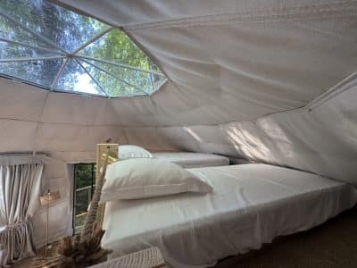 Dôme géodésique lumineux avec lits confortables, offrant une vue sur la nature environnante.