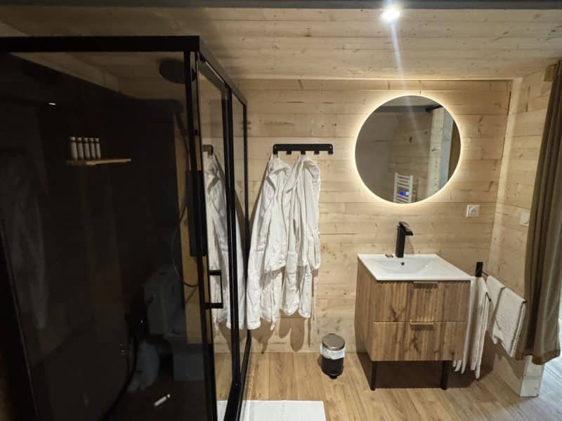 Salle de bain moderne dans un chalet, avec douche vitrée et éclairage doux.
