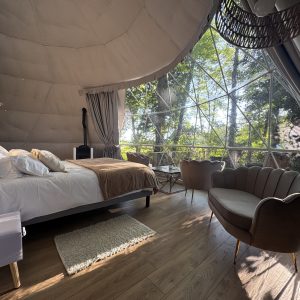 Dôme transparent avec lit douillet et vue sur la nature, ambiance moderne et chaleureuse.