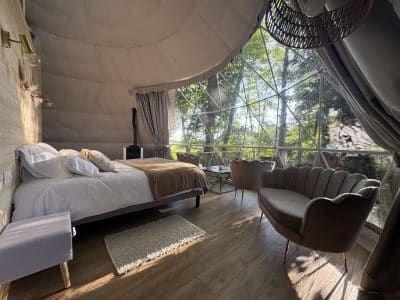 Dôme transparent avec lit douillet et vue sur la nature, ambiance moderne et chaleureuse.