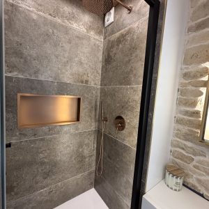 Douche moderne en pierre grise dans un hébergement insolite, avec robinetterie dorée.