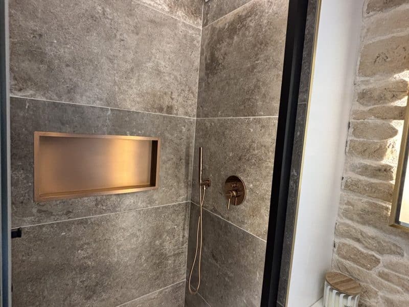 Douche moderne dans un hébergement de luxe, avec carrelage gris et robinetterie dorée.