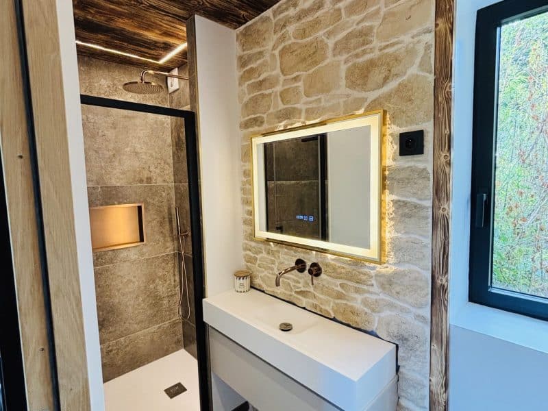 Salle de bain moderne dans un chalet, avec douche en verre et murs en pierre.