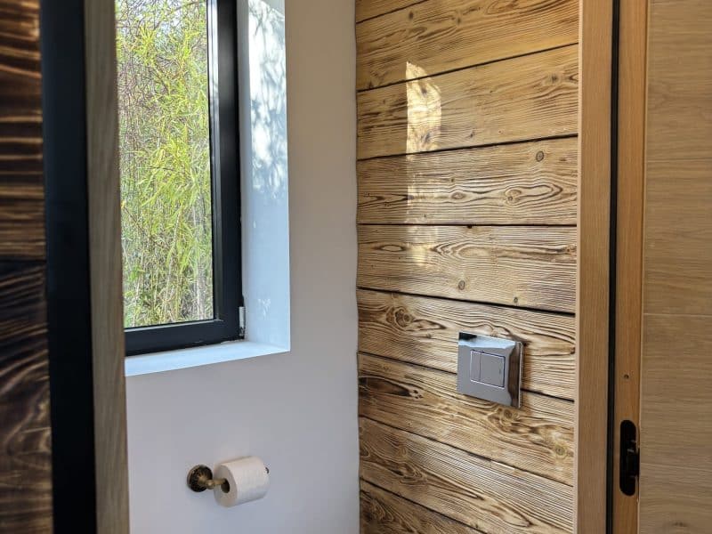 Toilettes modernes en bois, lumineuses grâce à une fenêtre donnant sur la nature.