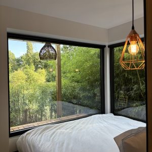 Chambre moderne avec grandes fenêtres, vue sur un jardin verdoyant et ambiance chaleureuse.