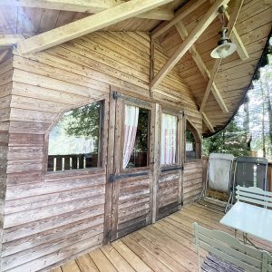 Charmante cabane en bois avec terrasse, entourée de verdure et baignée de lumière naturelle.