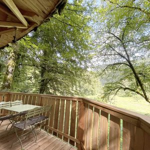 Cabane en bois perchée, avec terrasse en bois et vue sur la verdure environnante.