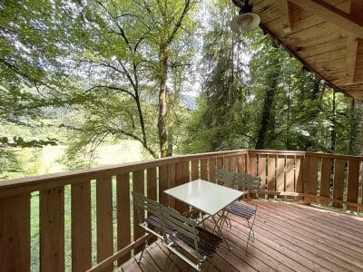 Cabane en bois avec terrasse ensoleillée, entourée d'une forêt verdoyante.