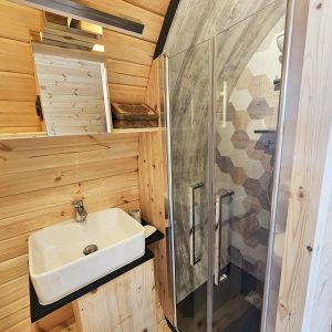 Salle de bain en bois dans un hébergement insolite, avec douche à l'italienne et lavabo moderne.