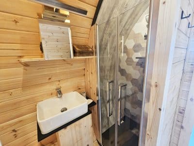 Salle de bain en bois dans un hébergement insolite, avec douche à l'italienne et lavabo moderne.
