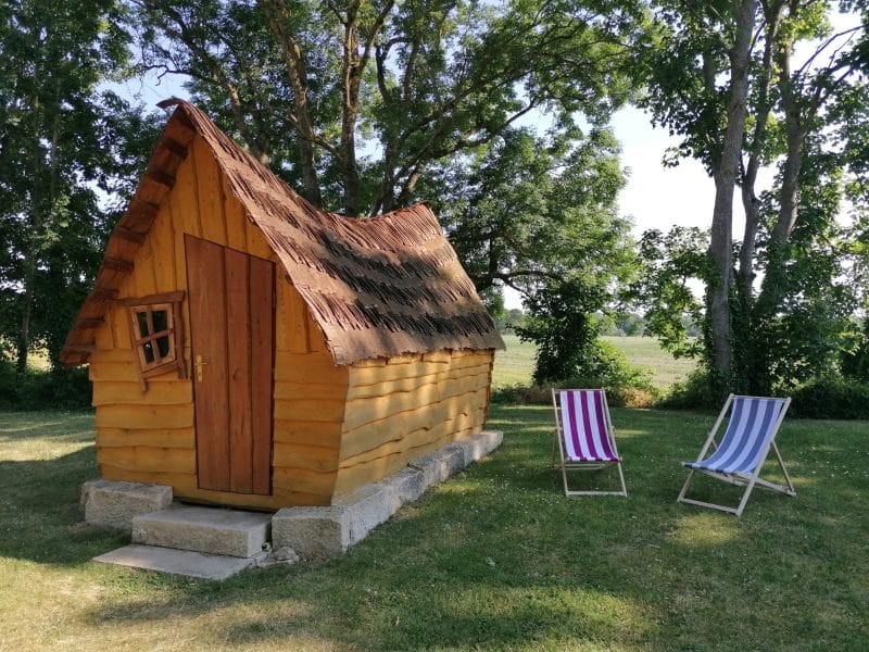 Cabane en bois avec toit en chaume, entourée de chaises longues sur la pelouse.