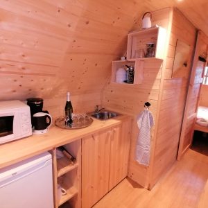 Intérieur d'un chalet en bois, avec kitchenette équipée et lit douillet. Ambiance chaleureuse.