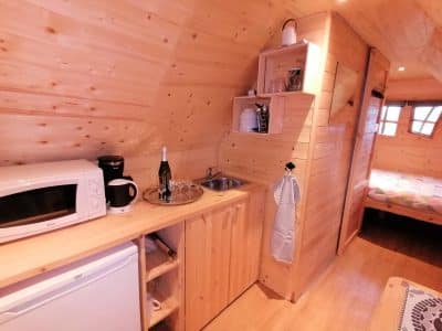 Intérieur d'un chalet en bois, avec kitchenette équipée et lit douillet. Ambiance chaleureuse.
