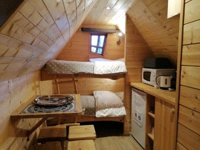 Cabane en bois cosy avec lits superposés, kitchenette et ambiance chaleureuse.