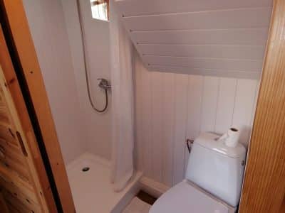Salle de bain d'un hébergement insolite, avec douche et toilettes modernes sous un toit mansardé.