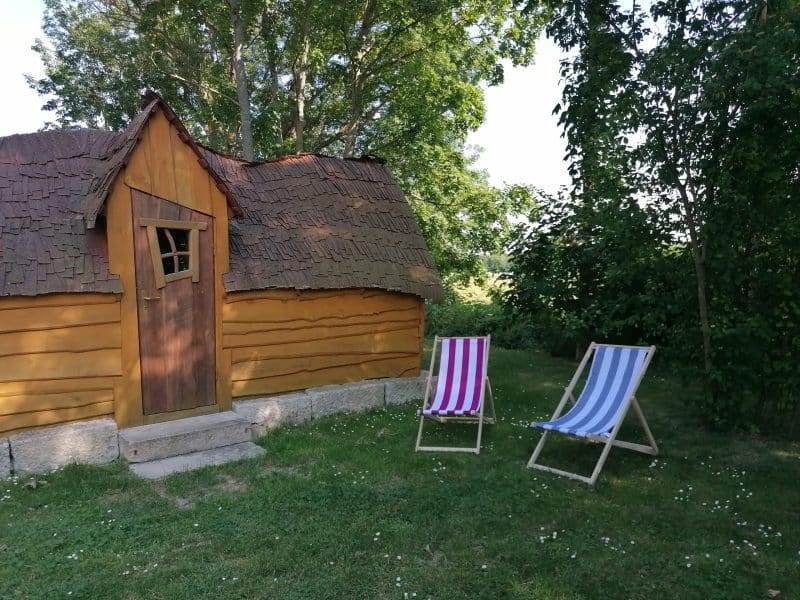 Charmante cabane en bois avec chaises longues colorées dans un cadre verdoyant.