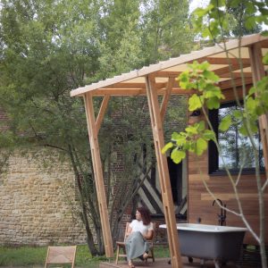 Cabane en bois avec baignoire extérieure, entourée de verdure apaisante.